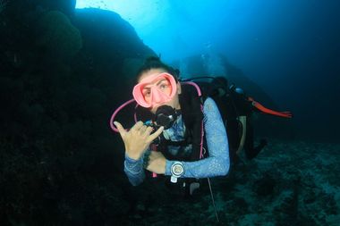 Duiker met roze masker maakt een shaka-teken onder water.
